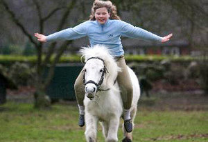 Ein glückliches Kind reitet ohne Sattel auf einem kleinen weißen Pony und streckt die Arme aus, während es reitet.